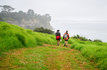 Two women walking the Long Bay coastal Okura Track in the rain. Cliff and trees in the mist. Auckland.