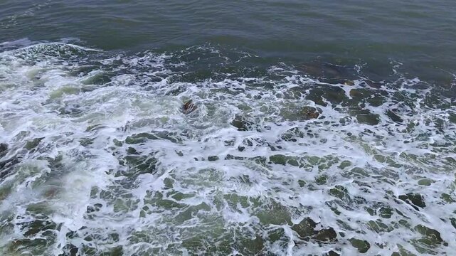 Small sea water waves hitting to brown stones, daylight, full HD
