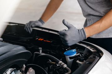 Hand of client showing thumb up for approval of car repair work, Mechanic working under the hood of car.
