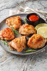 Chicken thighs baked with rosemary, lemon juice and zest close-up in a plate on the table. Vertical