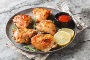 Marinated and then baked chicken thighs with lemon and rosemary served with ketchup close-up in a plate on the table. Horizontal