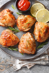 Traditional baked chicken thighs with lemon and rosemary served with tomato sauce close-up in a plate on the table. Vertical top view from above