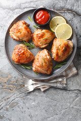 Chicken thighs baked with rosemary, lemon juice and zest close-up in a plate on the table. Vertical top view from above