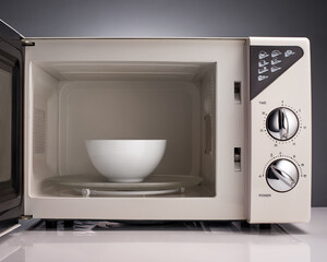 Fototapeta premium White open microwave with bowl on gray background