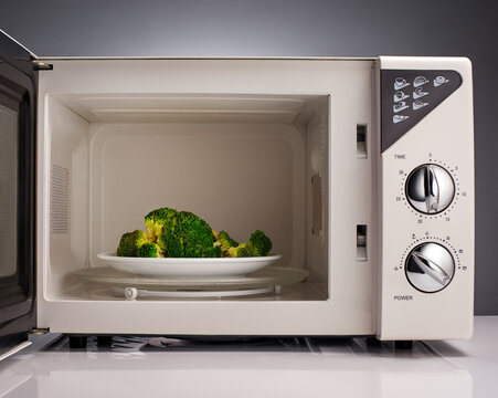 Cooked broccoli on white plate in open microwave
