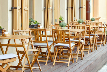 Vacant terrace scene with wooden tables and chairs, empty outdoor patio in summer,  restaurant relaxation space. Reastaurant tables waiting for customers at an outdoor terrace.