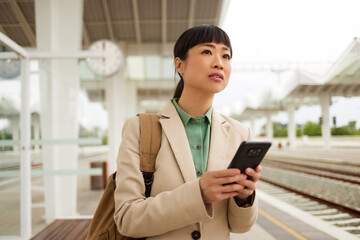 Asian businesswoman with smart phone waiting for the train at the train station