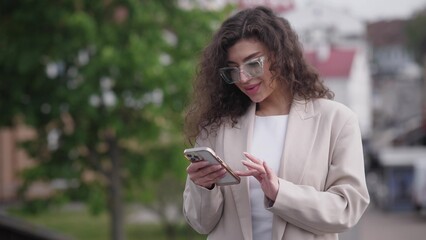 beautiful stylish white woman with curly hair in the summer with a phone in her hands communicates on social networks with her friends