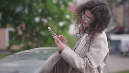 beautiful stylish white woman with curly hair in the summer with a phone in her hands communicates on social networks with her friends