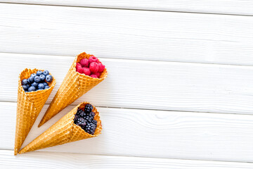 Summer breakfast with fresh berries in waffle cones on white woo