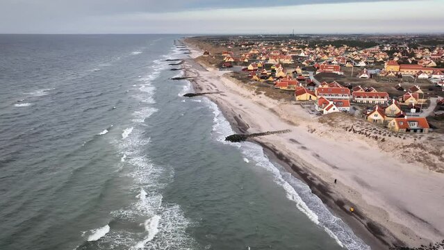 Dune landscape with a view of the village of Gammel Skagen, featuring houses painted in yellow with characteristic red roofing.Walk along North Sea coastal landscape, featuring a sandy shore and waves