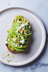 Avocado toast with feta and pistachio on plate, white marble background.