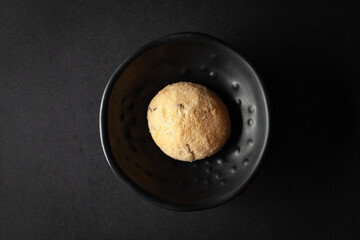 piece of coconut butter bakery cookie, placed in a black bowl on a black background.