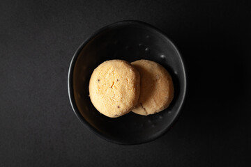 piece of coconut butter bakery cookie, placed in a black bowl on a black background.