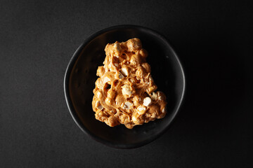 piece of Chickpea (chana dal) chikki, placed in a black bowl on a black background.