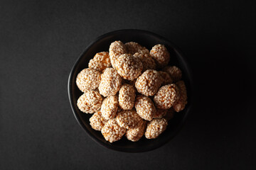 Top view of a black bowl filled with Indian sweet item called 'Rewri' or 'Revdi' or Sesame seeds sweet, on a black background.