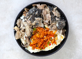 Flat lay of Traditional South African Mogodo or tripe and innards stew with pap and chakalaka in a black bowl on grey with copy space