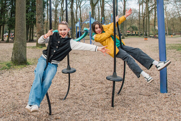 Obraz premium Cheerful teenage girls on hanging swings in the park