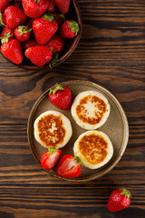 Cheesecakes, syrniki, cheese pancakes with strawberries, cashew and tofu on a wooden table. Sugar, lactose and gluten free. Vertical orientation, top view.