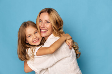 Joyful mother and daughter embracing with smiles on a vibrant blue background, expressing love and...