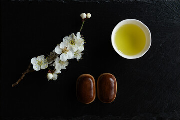 Manju, Traditional Japanese sweets, Ume (apricot) flower branch and Japanese green tea in a beauty minimalist aesthetic arrangement on black granite board background. Japan.