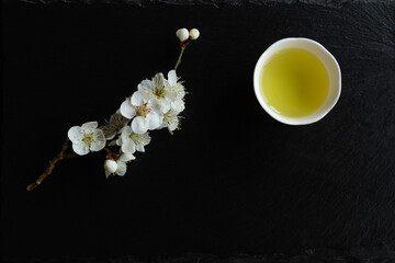 Japanese green tea and Ume (apricot) flowers in a beauty minimalist aesthetic arrangement on black granite board background. Japan.