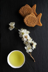 Taiyaki, Traditional Japanese sweets, Ume (apricot) flower branch and Japanese green tea in a beauty minimalist aesthetic arrangement on black granite board background. Japan.