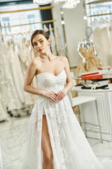 Naklejka premium Young brunette bride in a white dress gazes at her reflection in a mirror in a wedding salon, embodying elegance and grace.