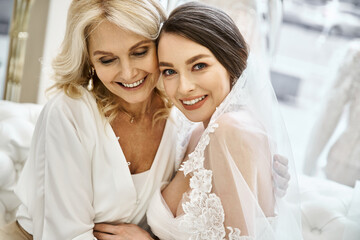 Naklejka premium A young brunette bride in a wedding dress and her middle-aged blonde mother stand side by side in a bridal salon.