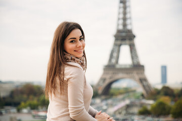 Beautiful girl posing to the photographer against the background of the Eiffel Tower. Sunny weather. Beautiful smile and makeup