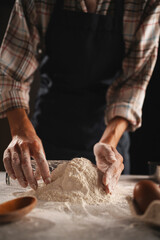 Baker's hands scooping flour into glass on table, plaid shirt, dark background
