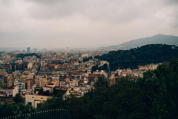 Fototapeta premium A panoramic view captures an urban cityscape nestled between mountains, dense buildings under a cloudy sky