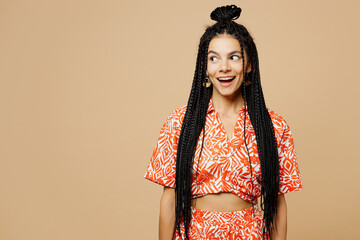 Young shocked surprised amazed overjoyed fun Latin woman she wears orange casual clothes look aside on area mockup isolated on plain pastel light beige background studio portrait. Lifestyle concept.