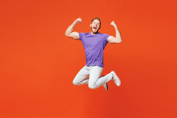Full body young exultant excited cool fun overjoyed happy man he wearing purple t-shirt casual clothes jump high do winner gesture isolated on red orange background studio portrait. Lifestyle concept.