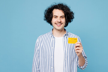 Young smiling happy fun man he wear shirt white t-shirt casual clothes hold in hand mock up of credit bank card isolated on plain pastel light blue cyan background studio portrait. Lifestyle concept.