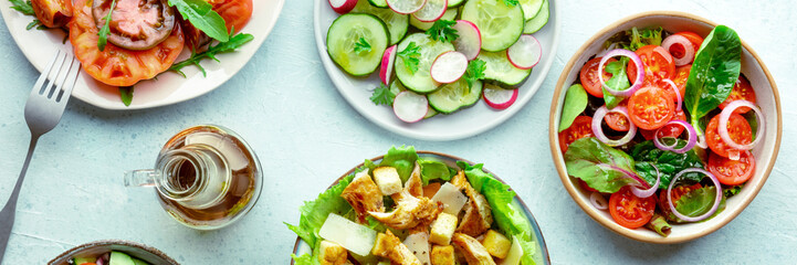 Fresh salads panorama, overhead flat lay shot of an assortment. Variety of plates and bowls with green vegetables. Healthy food, top shot, with olive oil