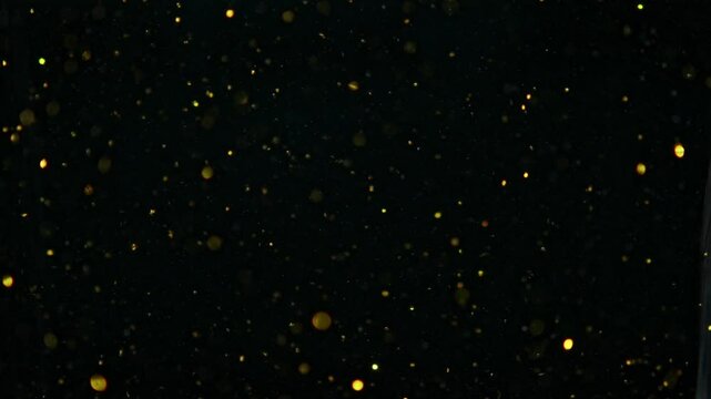 Small gold molecules glowing underwater, dark background, slowmo