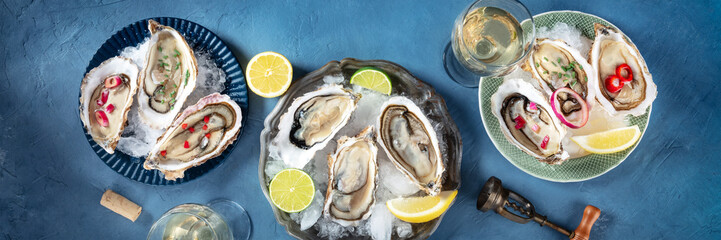 Oysters panorama on ice, with various toppings and white wine, overhead flat lay shot on a blue slate background