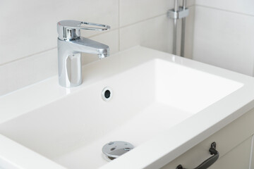 A drop of pure water dripping from the tap in the white modern bathroom. Clean tap water concept. Wise use of natural resources.