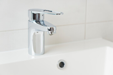 A drop of pure water dripping from the tap in the white modern bathroom. Clean tap water concept. Wise use of natural resources.
