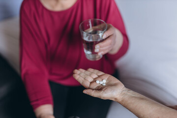 An elderly woman sits on her bed and a volunteer gives her pills and a glass of water