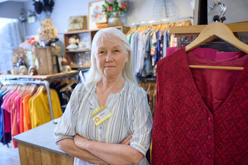 Portrait Of Senior Female Volunteer Working In Charity Shop Or Thrift Store Selling Used And Sustainable Clothing