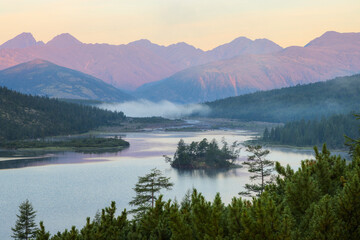 Morning landscape with a mountain lake. View of small islands covered with trees. Majestic mountains illuminated by the first rays of the sun at dawn. Lake of Dancing Graylings, Magadan Region, Russia