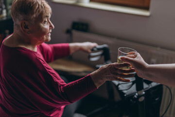 elderly woman, a disabled person with a walker for support, takes a glass of water