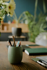 Close up photo of pastel green pencil cup with pencils and pens on top of wooden desk, defocused...