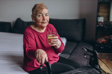 A lonely grandmother sits on her bed with a glass of water