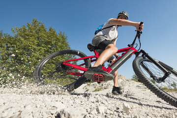 Male electric mountain bike rider going downhill and braking on a hilly rocky trail, low-angle...