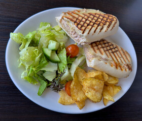 A tuna melt panini sandwich served on a white plate with crisps and green salad. 