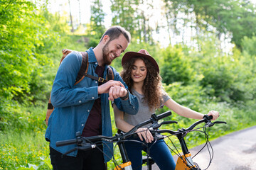 Fototapeta premium Travellers couple going on e-bike ride in nature. Tourist riding electric bicycles on easy trail road in the middle of forest. Young tourist spending summer vacation oudoors.