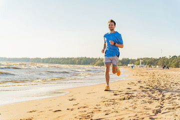 A man runs along a sunny beach near the waves, wearing a blue shirt and bright shoes, smiling as he jogs.